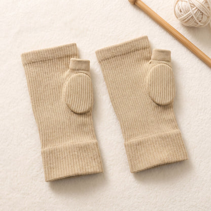 A pair of the thumb sleeves in beige laid flat, showing the cushioned oval pad over the thumb base and the ribbed cuff