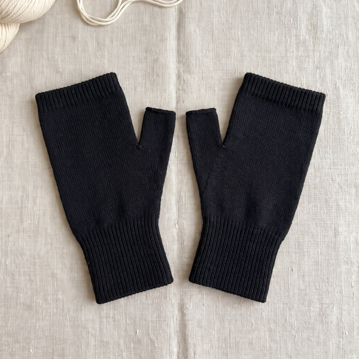 A pair of the thumb sleeves in black laid flat on linen, showing the thumb opening and ribbed cuff