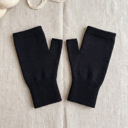 A pair of the thumb sleeves in black laid flat on linen, showing the thumb opening and ribbed cuff