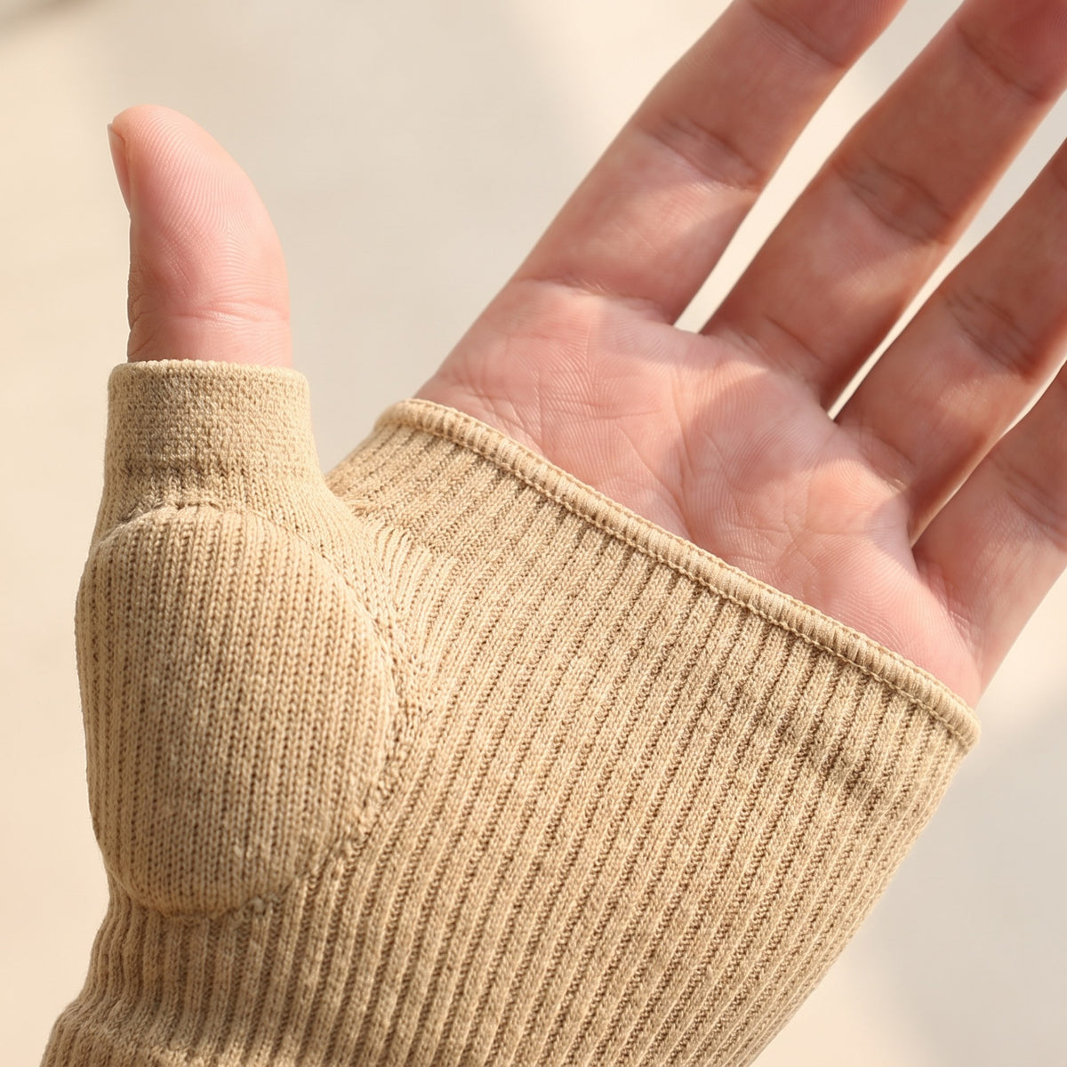 Close detail of the sleeve worn on a hand: the soft cushioned pad sitting over the base of the thumb, and the clean ribbed edge across the palm with all four fingers bare
